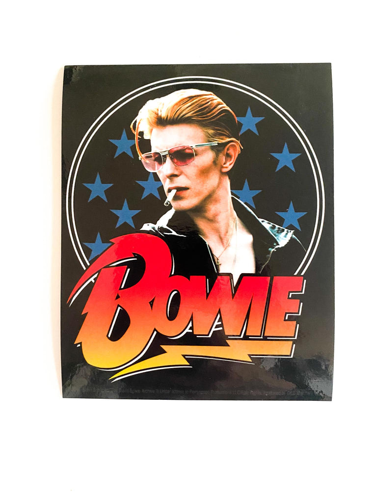 Officially licensed David Bowie stars sticker. Picture of David Bowie with sunglasses and a cigarette in his mouth. Blue stars in the background. The word "Bowie" in red.