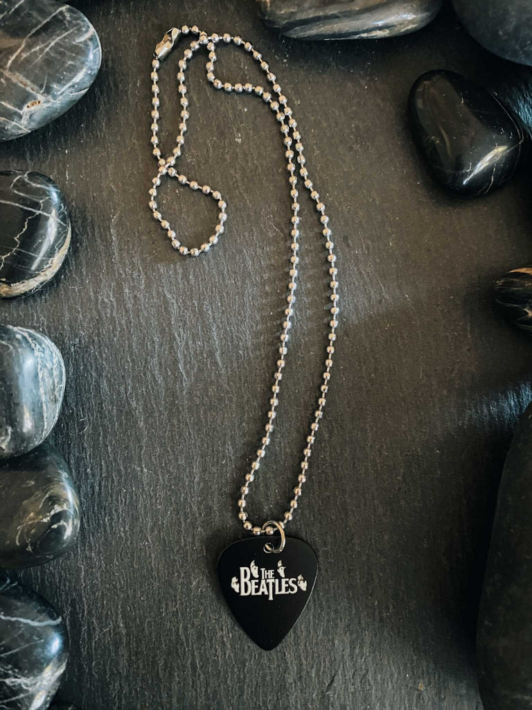 Beatles guitar pick necklace featuring their faces and the Beatles logo in white on a black guitar pick. Stainless steel ball chain. Band merch at Rock & Roll Jane.