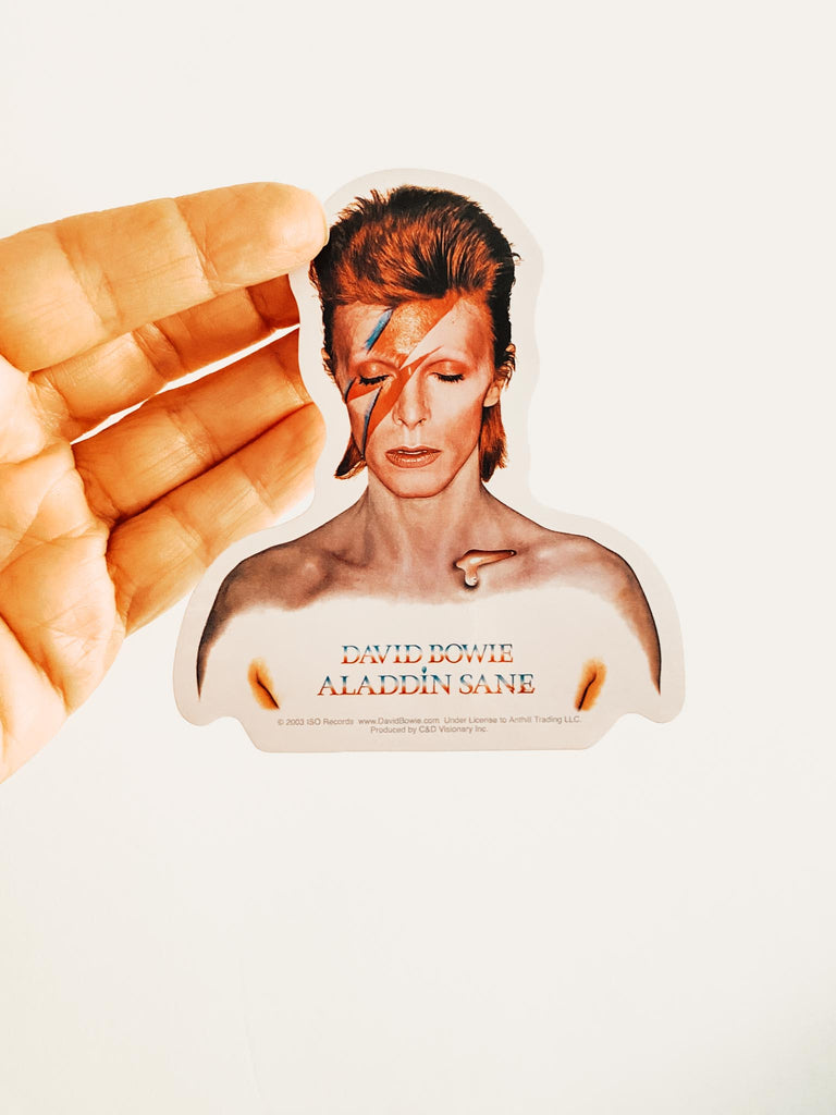 Sticker of David Bowie with 'Aladdin Sane' album text held by a hand. Official band merch available at Rock & Roll Jane.