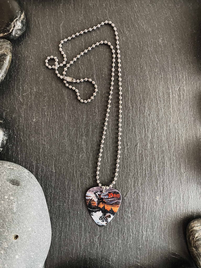 Ronnie James Dio guitar pick necklace with artwork from his "Holy Diver" album | 18" silver ball chain with extra cord included | Shop officially licensed band tees and band merch at Rock & Roll Jane