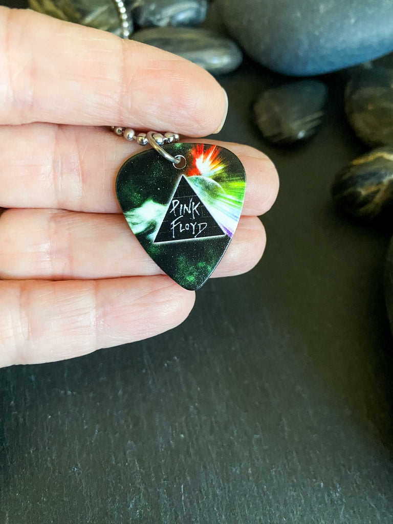 Pink Floyd guitar pick necklace made of stainless steel ball chain. The guitar pick features the Dark Side of the Moon prism and rainbow artwork. Guitar pick held on someone's hand.
