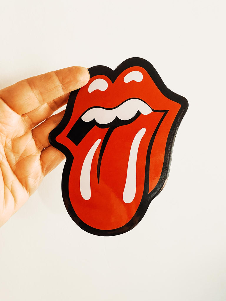 Sticker of a red mouth with a tongue sticking out, held by a hand against a white background. Rolling Stones logo sticker available at Rock & Roll Jane.