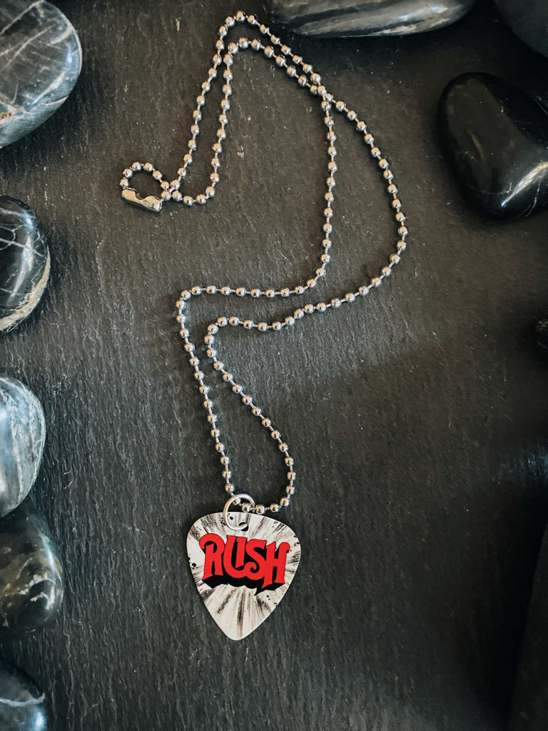 Rush guitar pick necklace on an 18" stainless steel ball chain. Band merch available at Rock & Roll Jane. Red logo lettering on a white and black background.