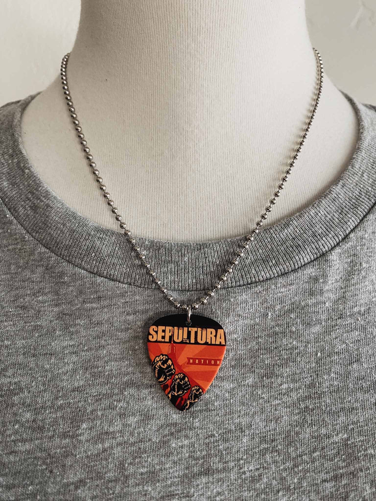 Sepultura guitar pick necklace | Artwork from the band's album, Nation | 18" silver ball chain | Made in the USA. Available at Rock & Roll Jane | officially licensed band tees and accessories