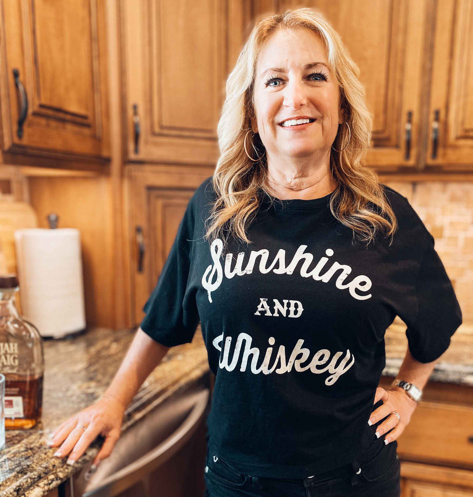 woman wearing black graphic t-shirt with words "Sunshine and Whiskey" on front | Rock & Roll Jane | Officially licensed band tees and more